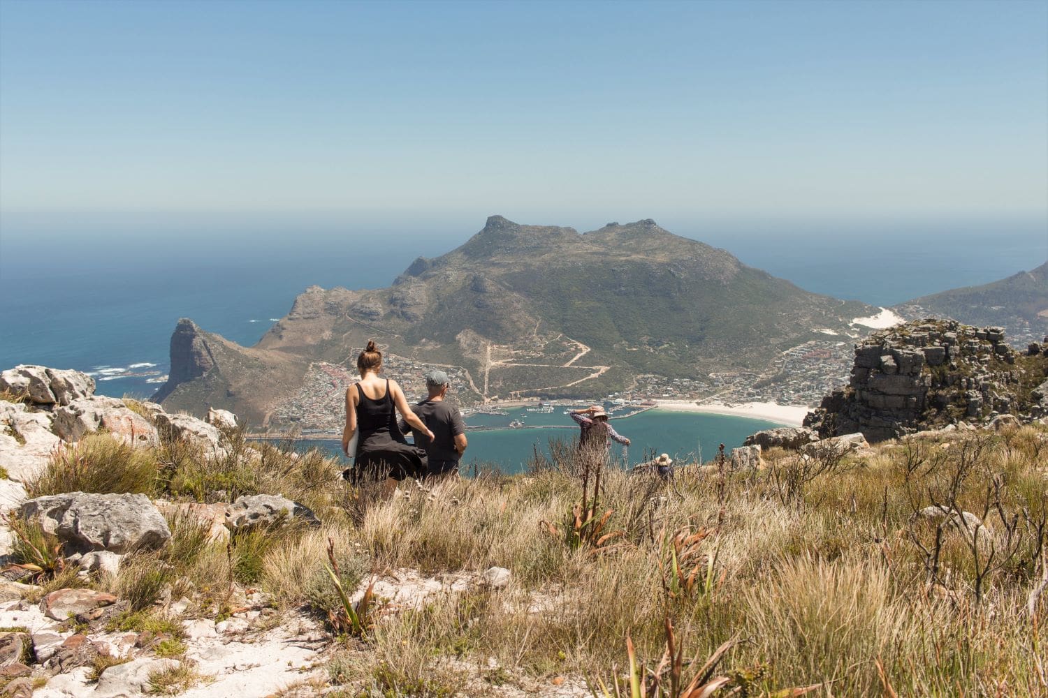 A group of people walking down a mountain with water an another mountain in front of them